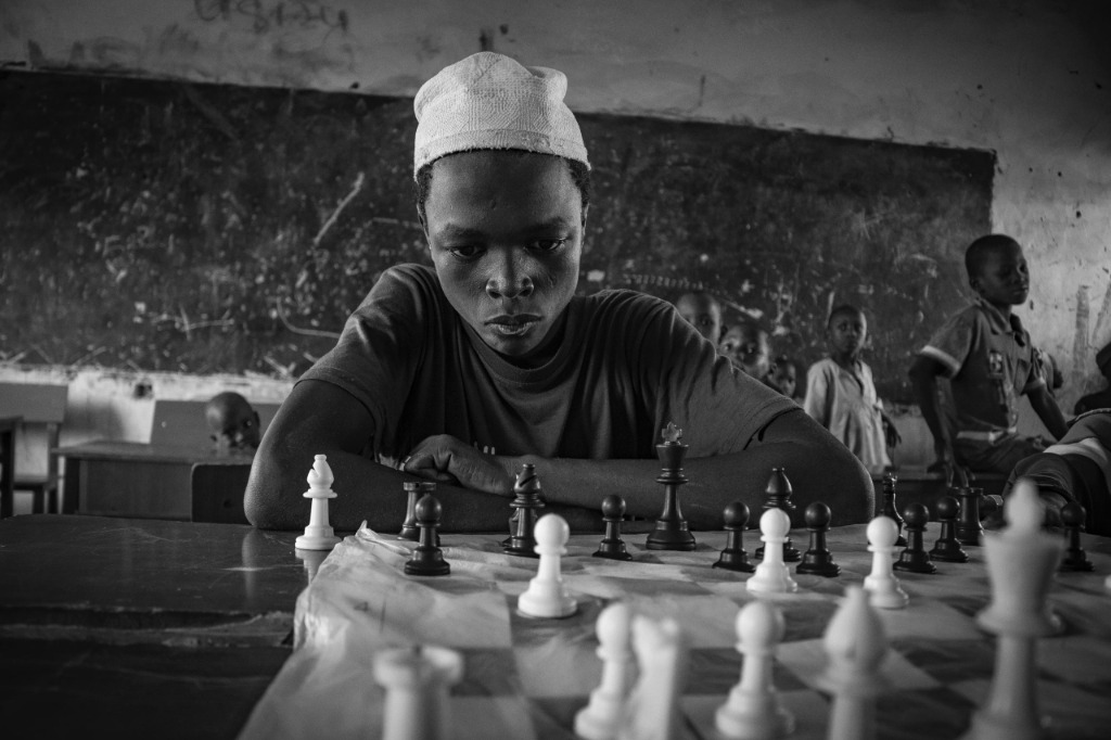 A child focusing deeply on a chess game in an IDP camp classroom