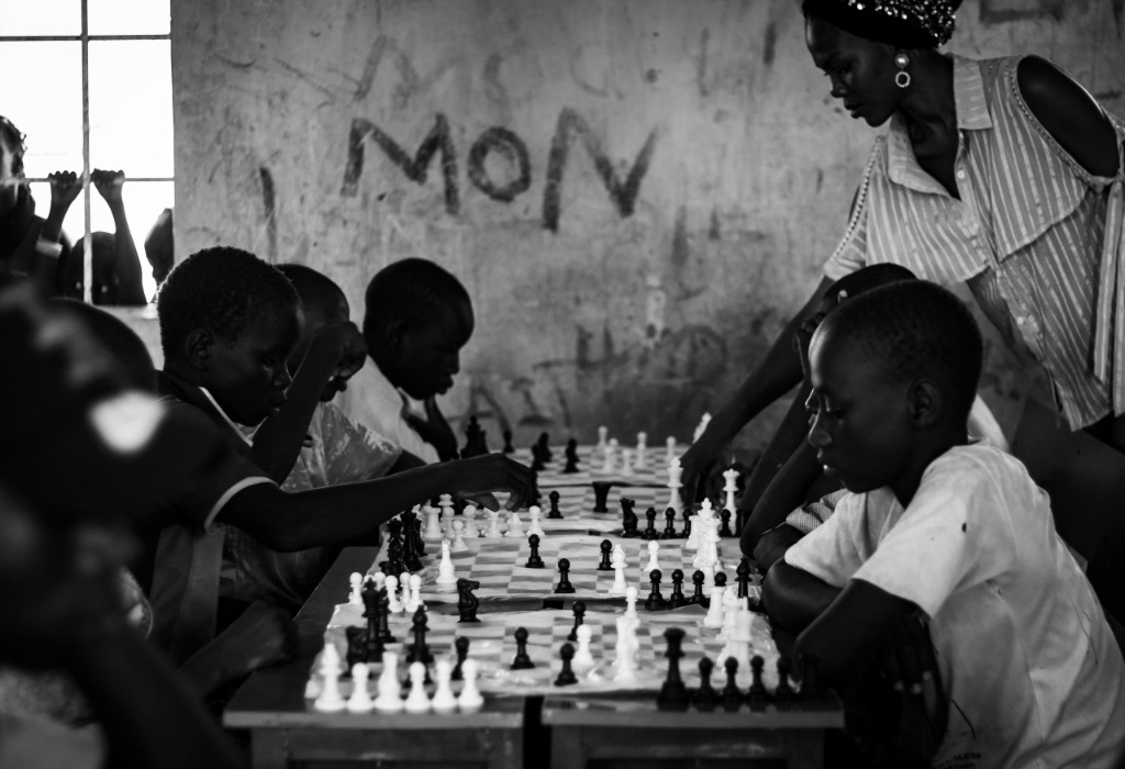 A row of multiple children playing chess under an instructor's guidance